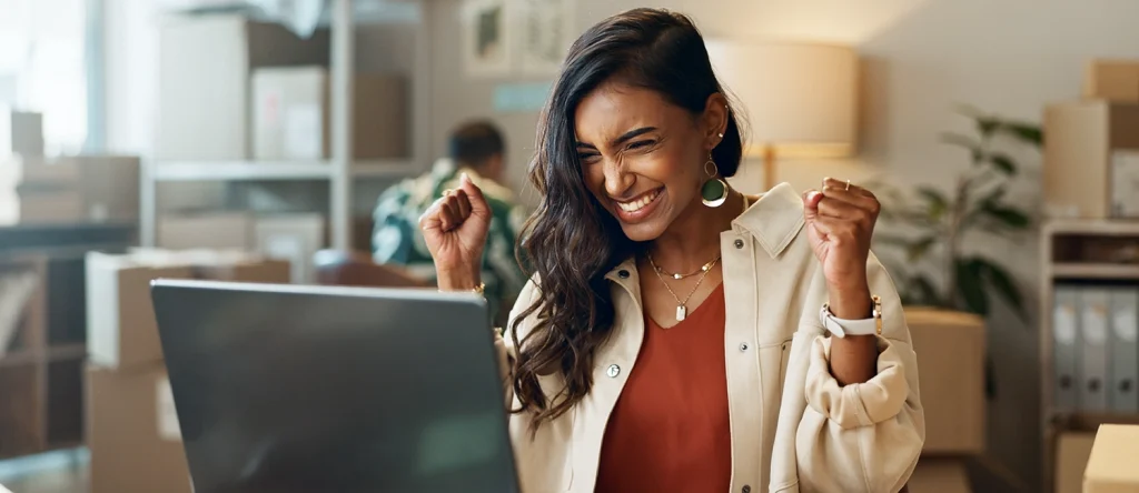 Mulher a festejar em frente ao computador, satisfeita com os benefícios da empresa